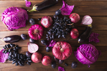 Purple fruits and vegetables. Blue onion, purple cabbage, eggplant, grapes and plums on a wooden background.