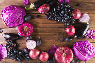 Purple fruits and vegetables. Blue onion, purple cabbage, eggplant, grapes and plums on a wooden background.
