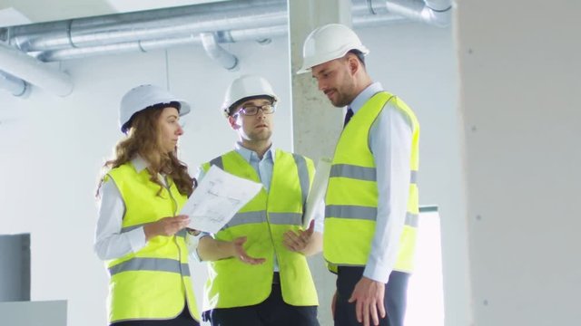 Team of Engineers in Hard Hats Having Conversation, Looking at Blueprint, inside Building Under Construction. Shot on RED Cinema Camera in 4K (UHD).