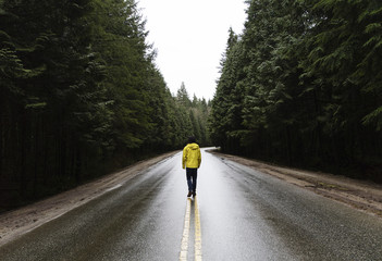 Person walking a road in the forest. Pacific North West, Vancouver British Columbia Canada. Straight road with evergreen trees on both sides. 