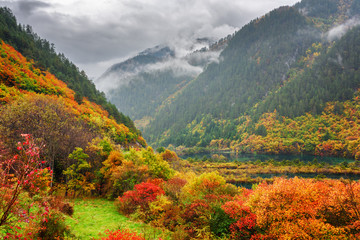 Beautiful view of mountains in fog, colorful fall forest and lak