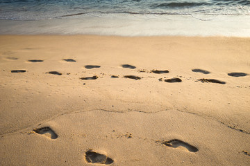 Blurred background image of footprints on sand beach along sea in the evening