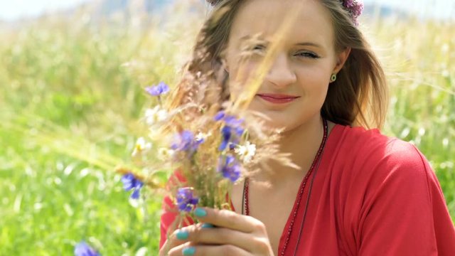 Girl with wreath of flowers sitting on the field and looking to the camera, steadycam shot
