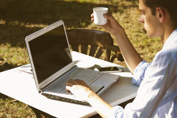 young man with laptop and coffee at sunset
