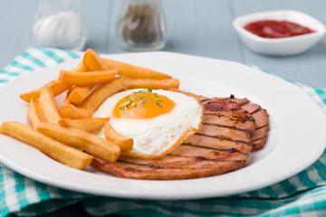 English breakfast with grilled ham, fried egg and french fries.