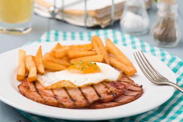 English breakfast with grilled ham, fried egg and french fries.
