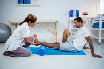 Physiotherapist doing leg therapy to a man using foam roll