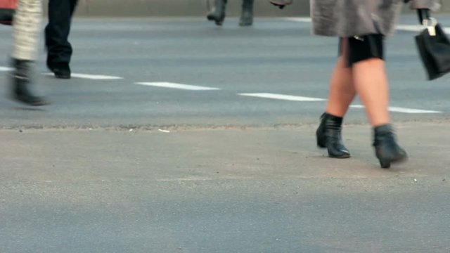 Legs of people who cross the street at a pedestrian crossing.