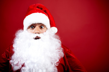 A portrait of Santa Claus looking at camera and surprised against red background