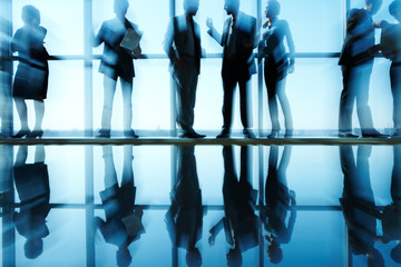 Silhouettes of business people lit from behind and their reflection in the floor