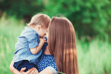 Loving mother holding son in her arms, plays with him and hugs him. Family rest on the nature. soft focus