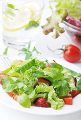 Fresh green salad with ripe tomatoes, pods of green peas and slices of strawberry.