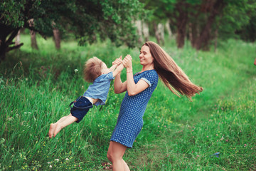 Fototapeta premium Loving mother holding son in her arms, plays with him and hugs him. Family rest on the nature. soft focus