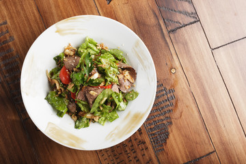 Salad with roast beef in a white plate. Brown wooden background