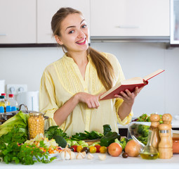 Happy young female with cookery book and veggies