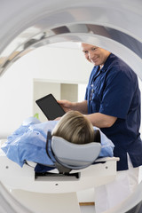 Doctor Showing Digital Tablet To Female Patient Undergoing CT Sc