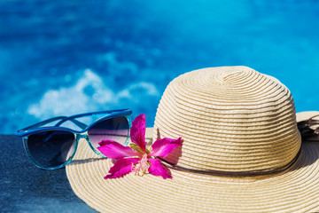 Sunglasses with flower and straw hat on a swimming pool