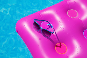 Sunglasses with pink mattress at the swimming pool