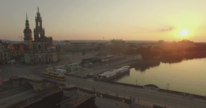 Aerial camera rises over the Elbe River with Katholische Hofkirche and the Augustusbruke in shot.The sun is setting in the background