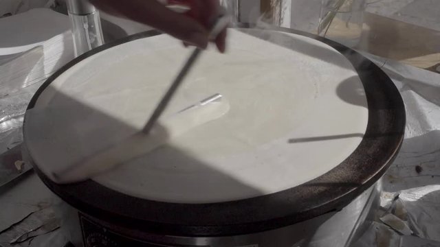 Dough on crepes / pancake maker being spread by T-shaped stick. SLOG3, medium shot.