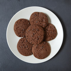 Aerial view of a plate of freshly baked chocolate chip cookies on a rustic slate background