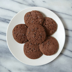 Aerial view of a plate of freshly baked chocolate chip cookies on a marble background