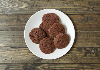Aerial view of a plate of chocolate chip biscuits on a rustic wooden counter top background