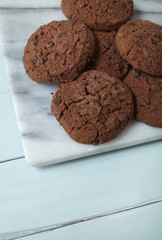 A pile of freshly baked chocolate chip biscuits on a marble and wood background forming a page border