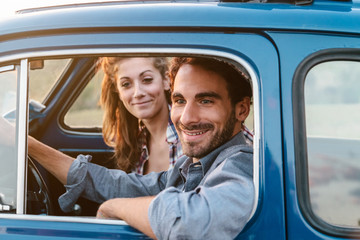 Loving couple in old blue car, young man is driving. Around classic landscape of Tuscany, Italy