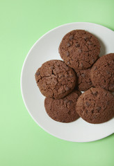 An aerial view of a plate of freshly baked chocolate chip cookies on a pastel green background
