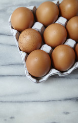 A tray of fresh brown chicken eggs on a marble counter top background