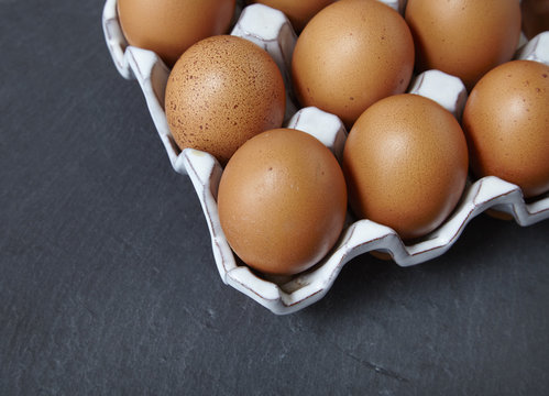 A tray of freshly laid chicken eggs on a rustic slate background
