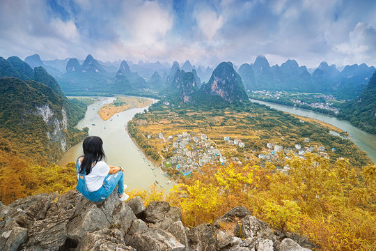 Chinesse woman sitting on the top of mountain and enjoing view on valley with rocks. Xing Ping, Yangshuo, China.