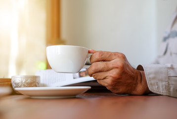 Man reading a book with white coffee cup in hand.