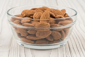 Almonds in a glass bowl on white old wooden table.