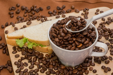 coffee beans on spoon and in cup with bread sandwich side by sid
