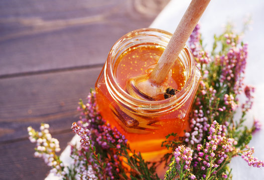 Honey in a glass jar with flowers melliferous herbs on a wooden surface. Honey with flowers of juniper