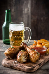 Roast chicken drumsticks, chips and beer on wooden table

