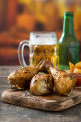 Roast chicken drumsticks, chips and beer on wooden table

