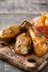 Roast chicken drumsticks and chips on wooden table

