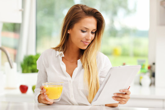 Young woman with orange juice and tablet in kitchen