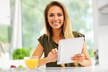 Young woman with orange juice and tablet in kitchen
