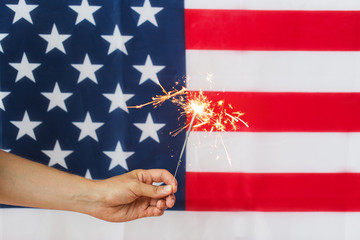 close up of hand with sparkler over american flag