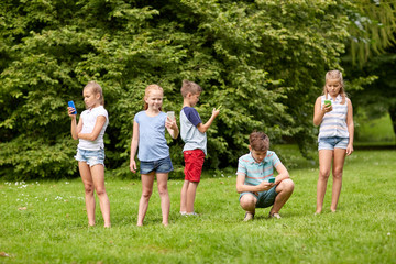 kids with smartphones playing game in summer park