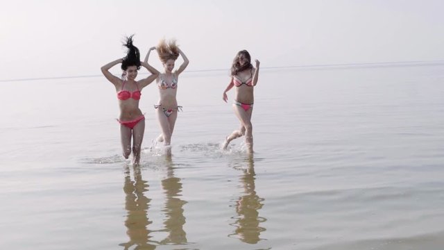 Group of mixed race girls running on the beach and smiling, in a stylish bikini enjoying summer vacation