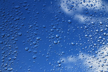 Rain drops on window with blue cloudy sky in background