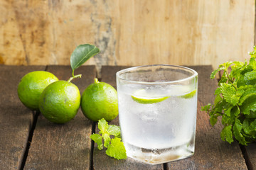 Lemonade in glass and green lemon on wooden background.Drink for health.Close up