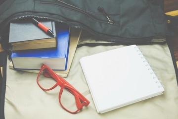 Top view of casual life style bag ; Old book,notebook,red glasses and casual shoes from inside bag.In Vintage tone