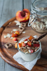 Yogurt topped with granola, sliced almonds, honey and chopped nectarines. Almond slices in a glass jar, nectarines on a wooden board.