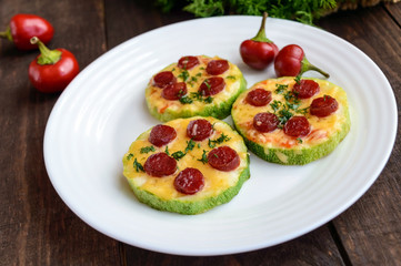 Small zucchini pizza on the circles with pepperoni and mozzarella. On a dark wooden background.